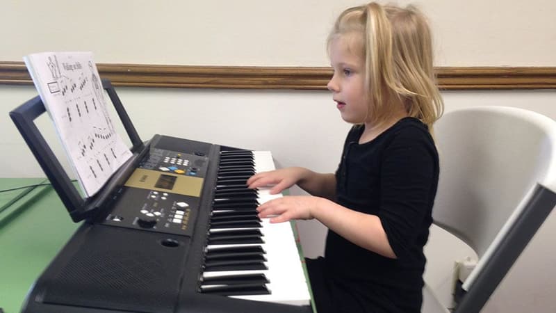 A young girl reading music and playing an electric keyboard with both hands.